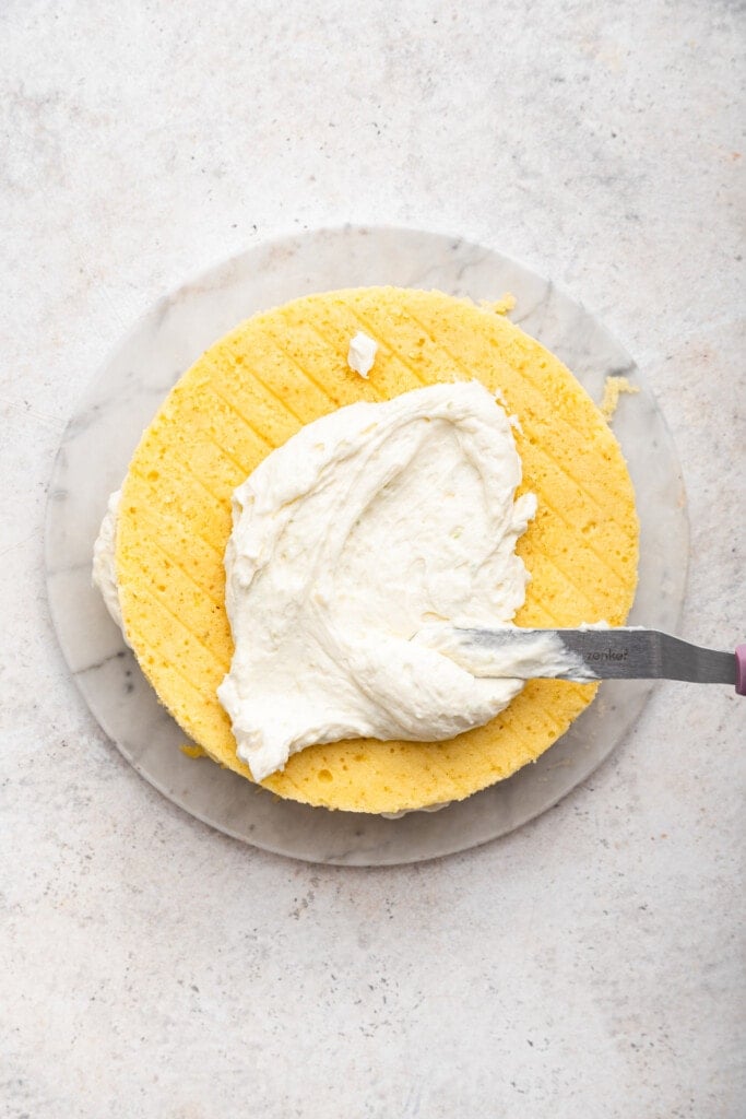 Spreading cream cheese frosting onto layer of cake