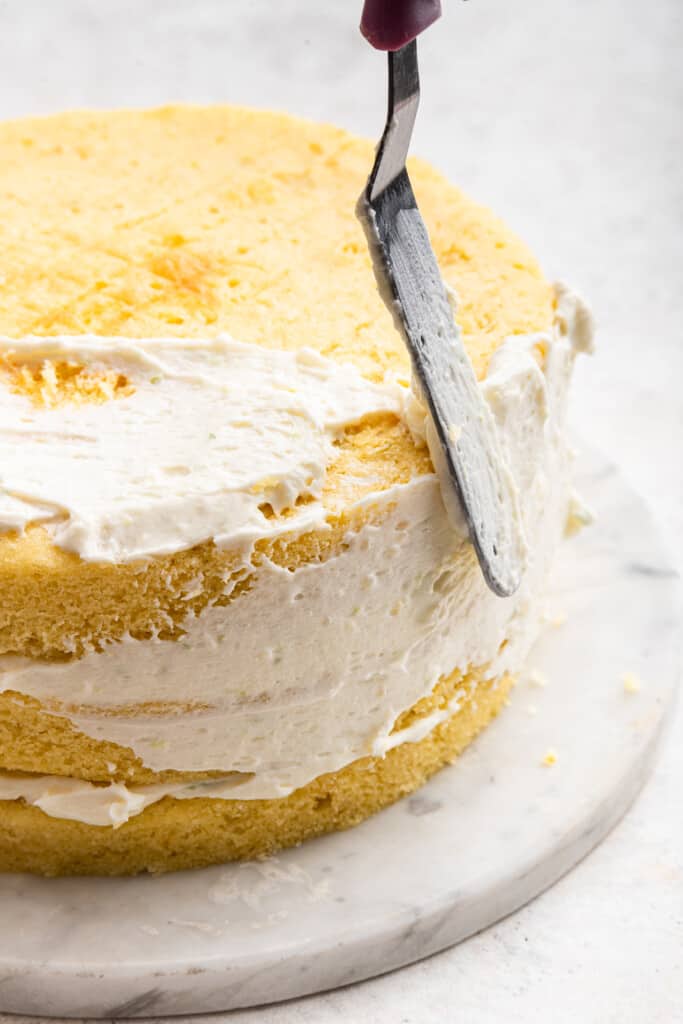 Using spatula to spread frosting onto key lime cake