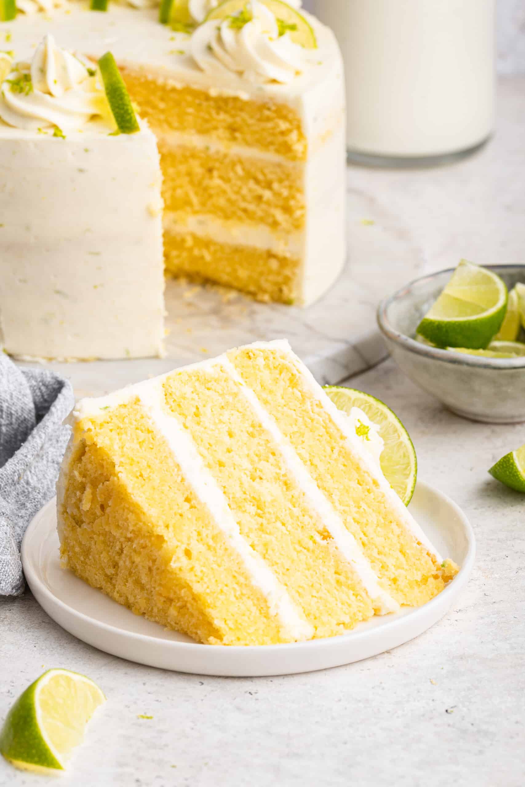 This key lime cake recipe is a stunning layer cake perfect for a party, with fluffy cream cheese frosting as the perfect finishing touch! Slice of key lime cake on plate