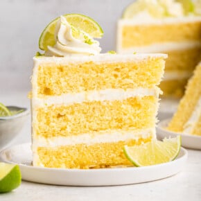 Slice of key lime cake on plate with lime slices
