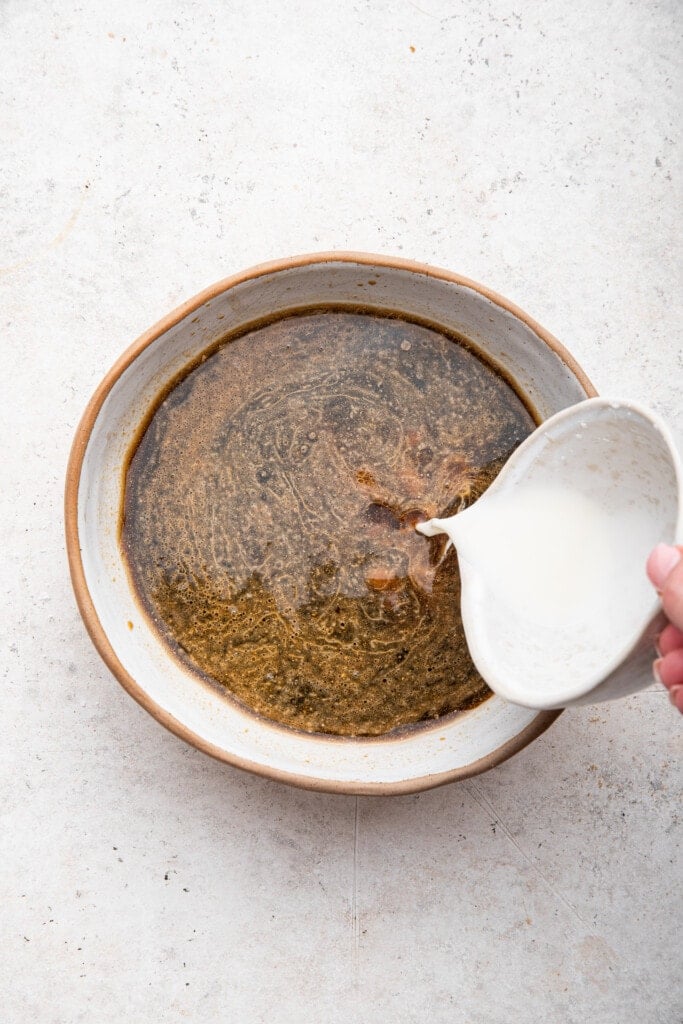 Pouring cornstarch slurry into sauce