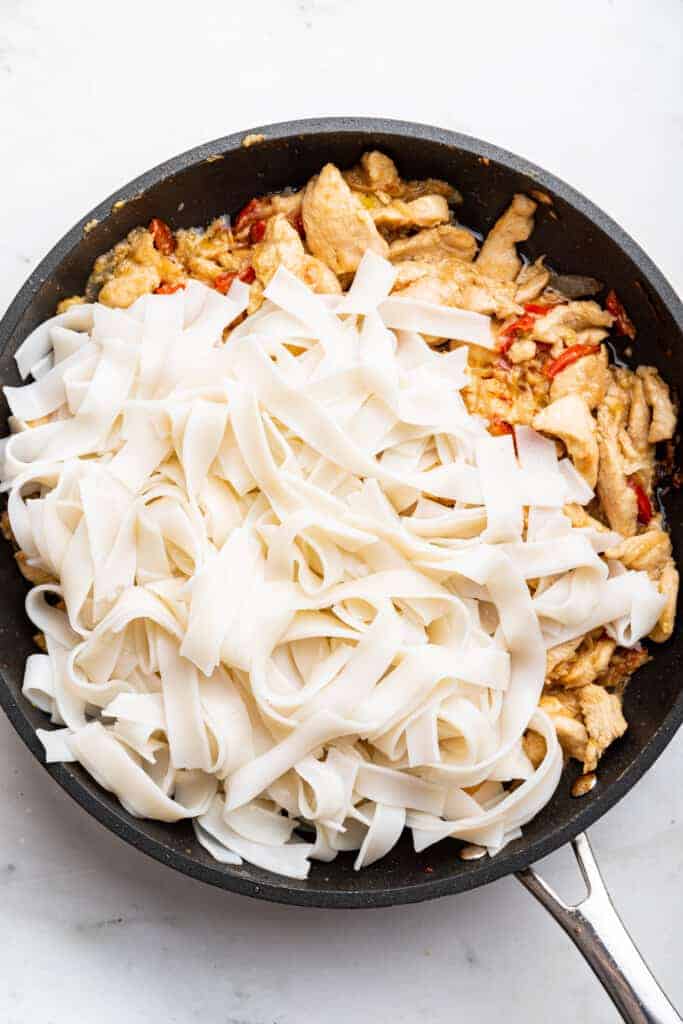 Rice noodles added to skillet of chicken and vegetables