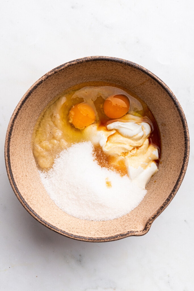 Overhead view of wet ingredients for banana bread in mixing bowl before stirring