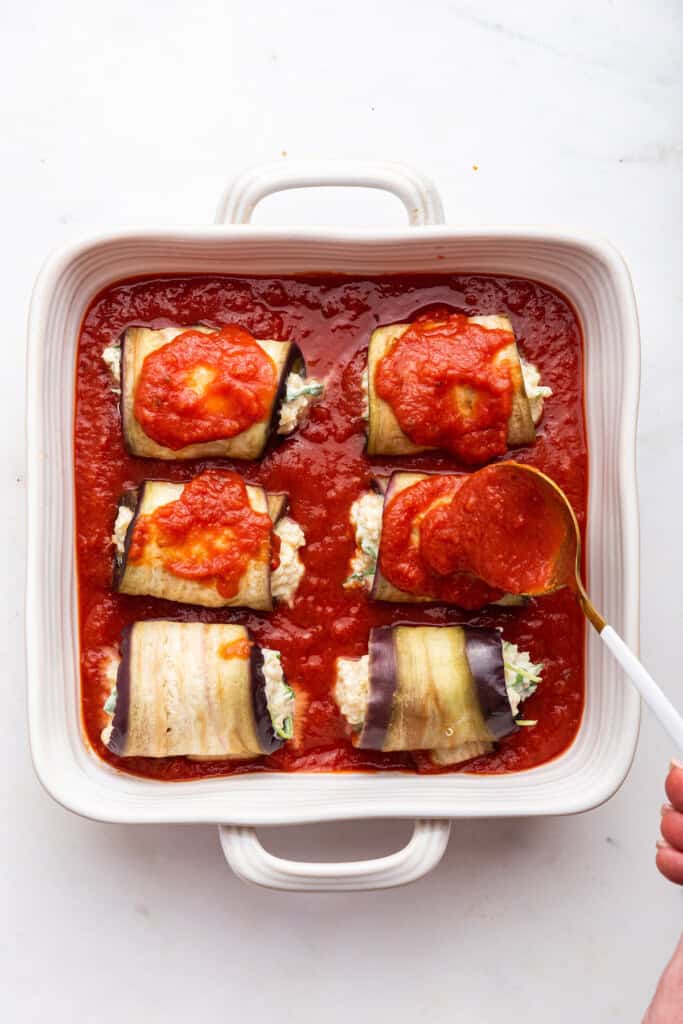 Spooning marinara over eggplant rolls