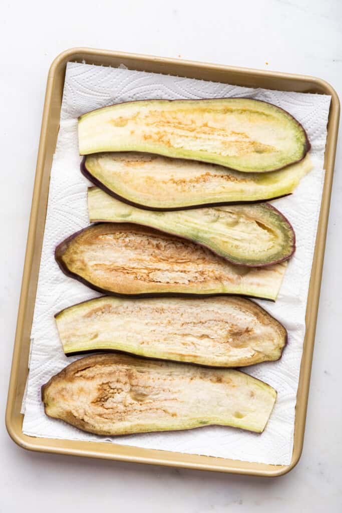 Overhead view of blanched eggplant slices on paper towel lined baking sheet