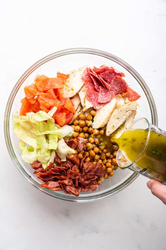 Pouring dressing into bowl with Jennifer Aniston salad ingredients