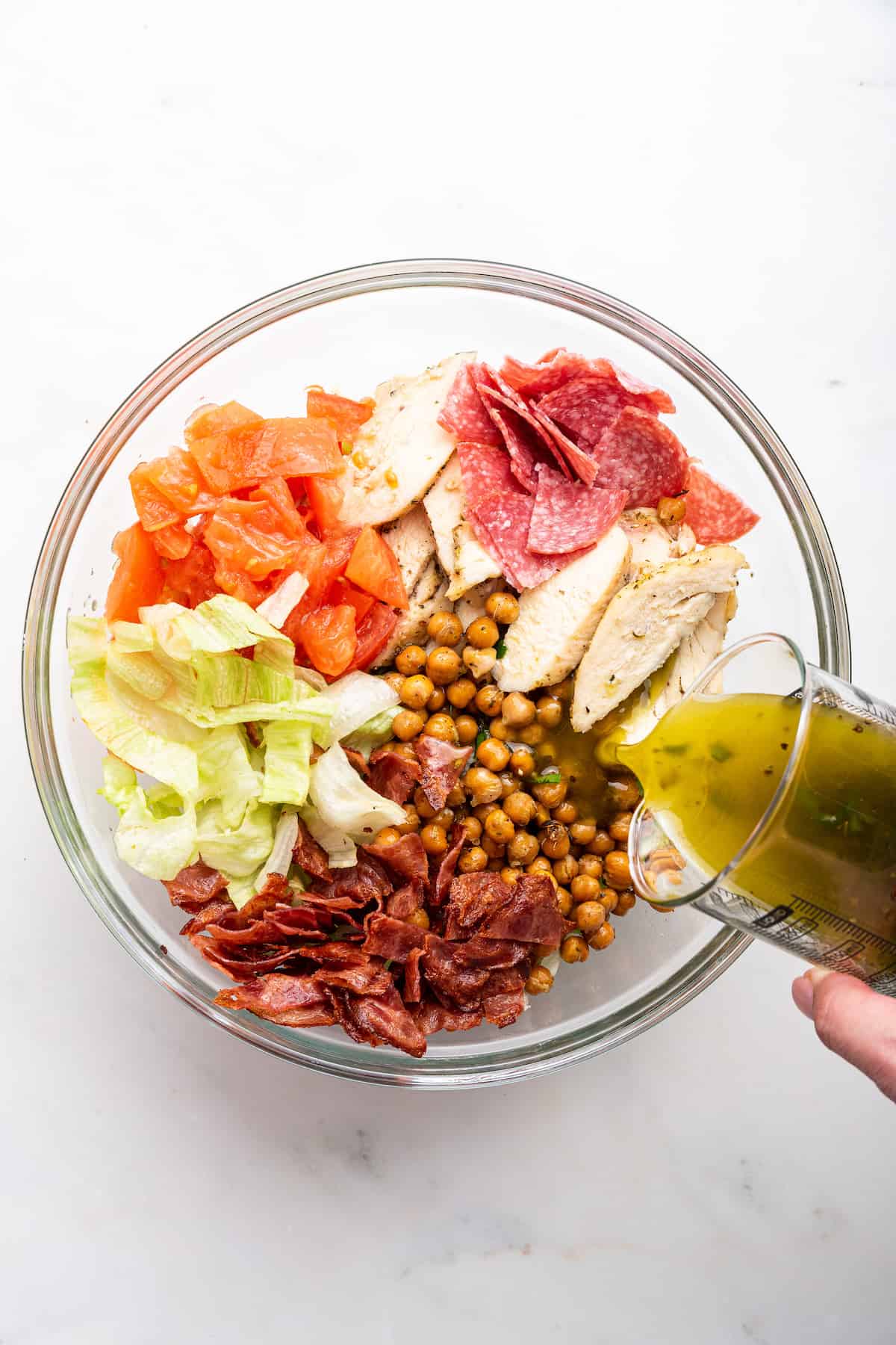 Pouring homemade salad dressing into bowl with Jennifer Aniston salad ingredients
