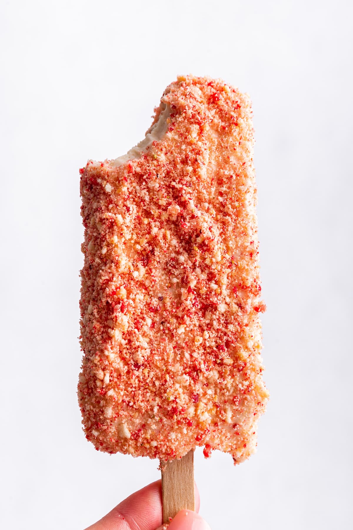 Strawberry shortcake ice cream bar with bite taken out of corner