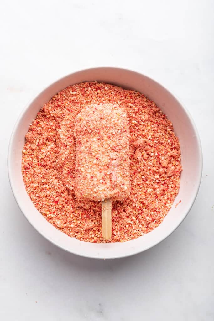 Dipping strawberry shortcake ice cream bar in crumb mixture