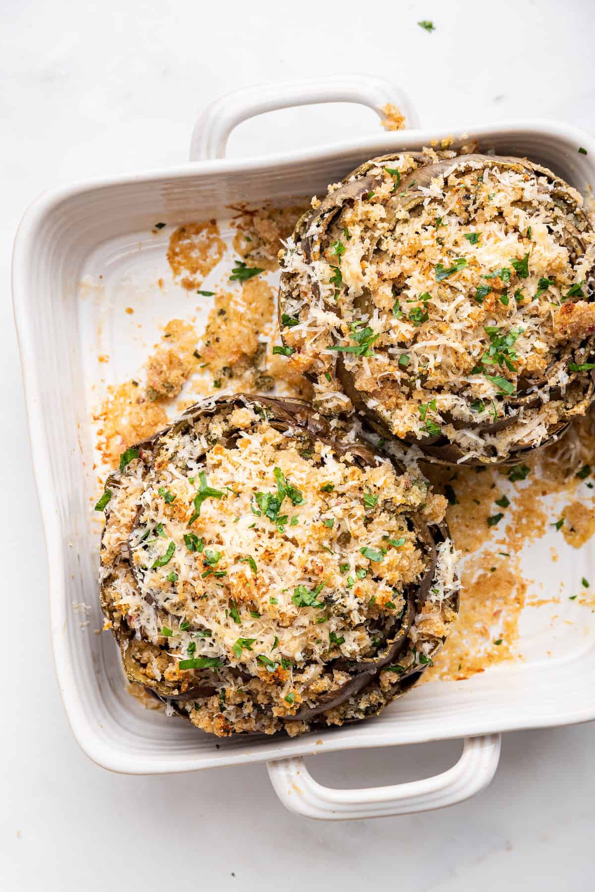 Overhead view of 2 stuffed artichokes in baking dish