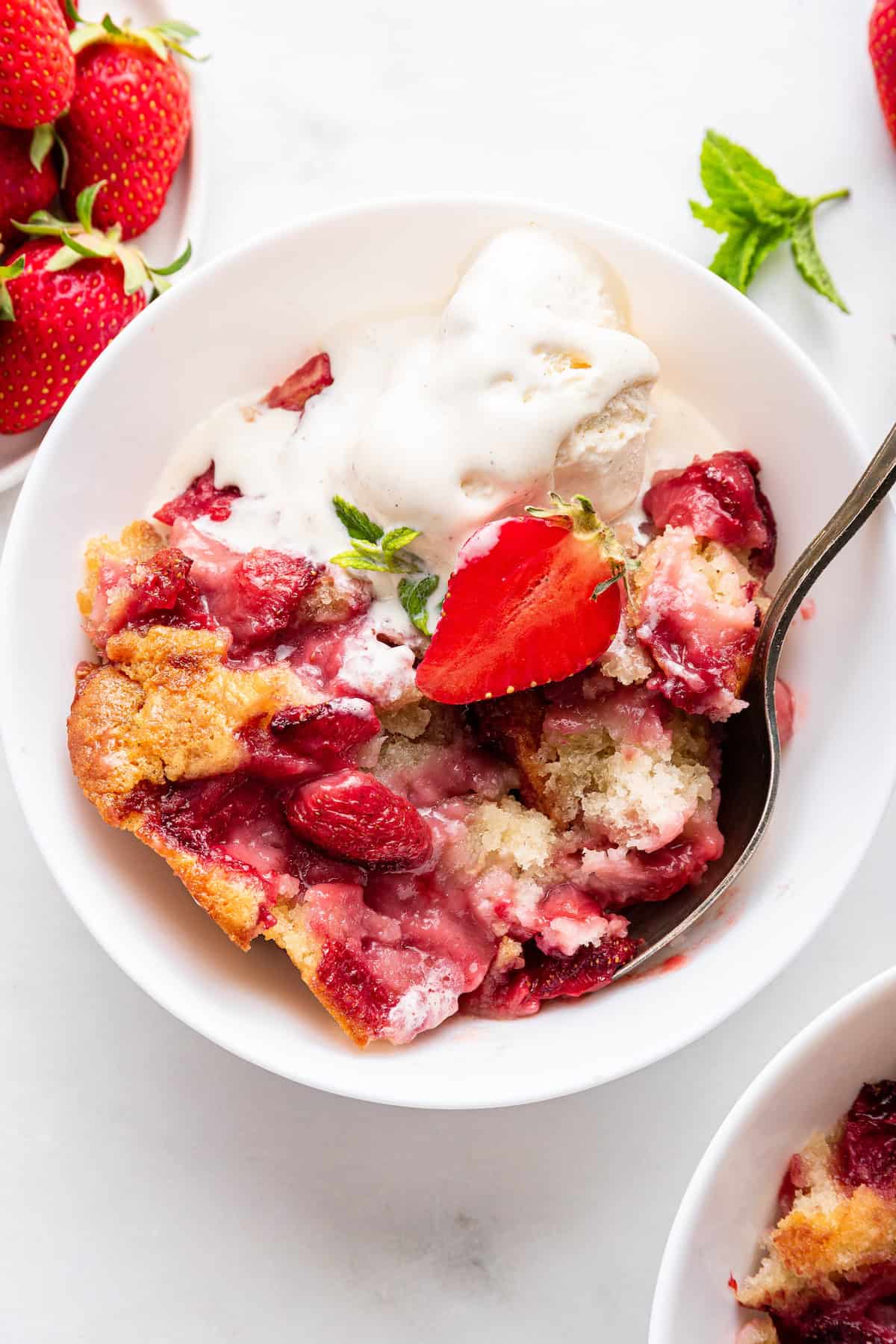 For a classic summer dessert, it’s hard to beat this old-fashioned strawberry cobbler recipe. Simple ingredients and a few minutes of prep! Strawberry cobbler in bowl with spoon and ice cream