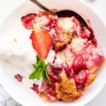 Overhead view of strawberry cobbler in bowl with spoon and scoop of ice cream