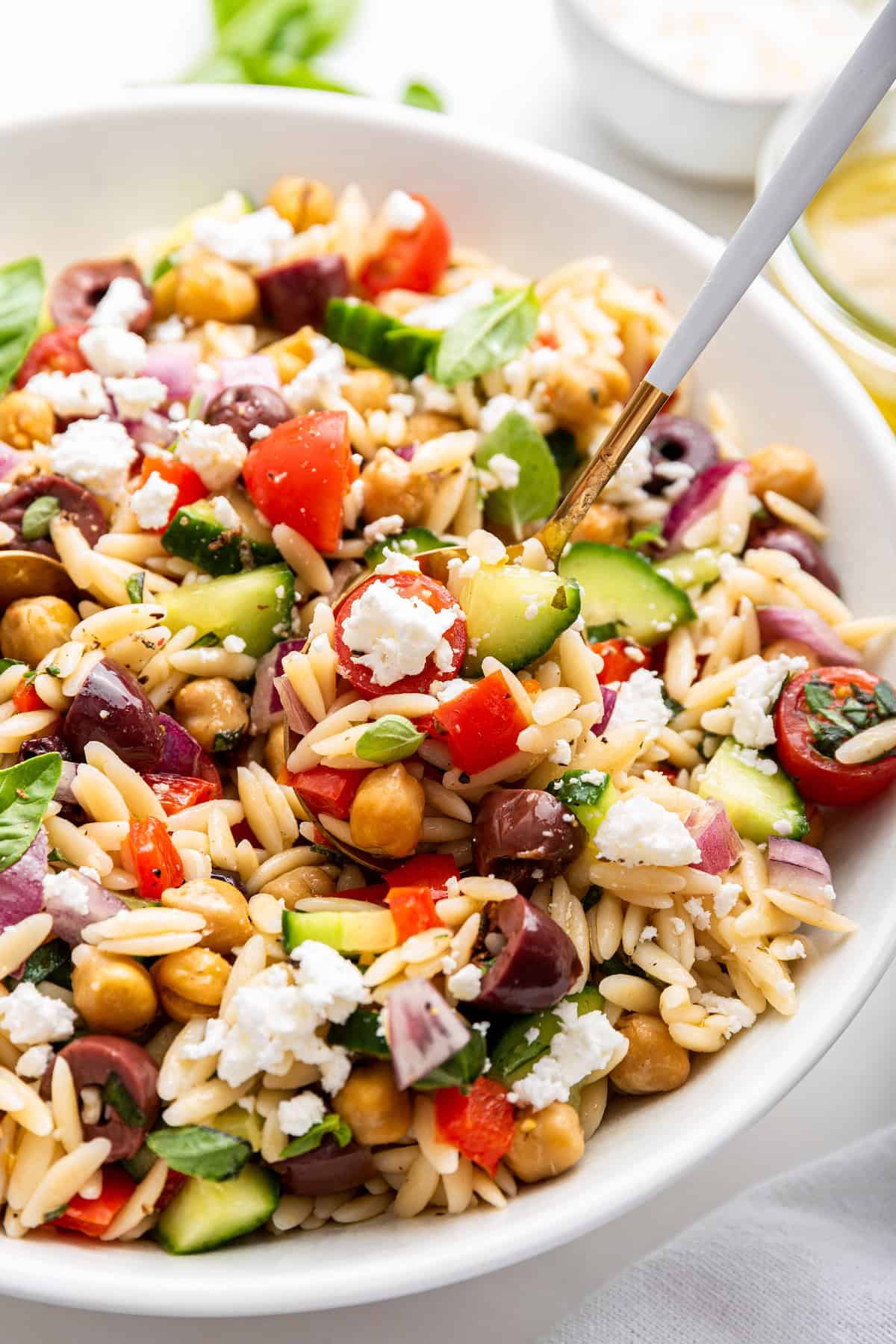 With bold Mediterranean flavors from olives, feta and roasted red peppers, this easy orzo pasta salad recipe is guaranteed to be a hit! Spoon digging into serving bowl of orzo pasta salad
