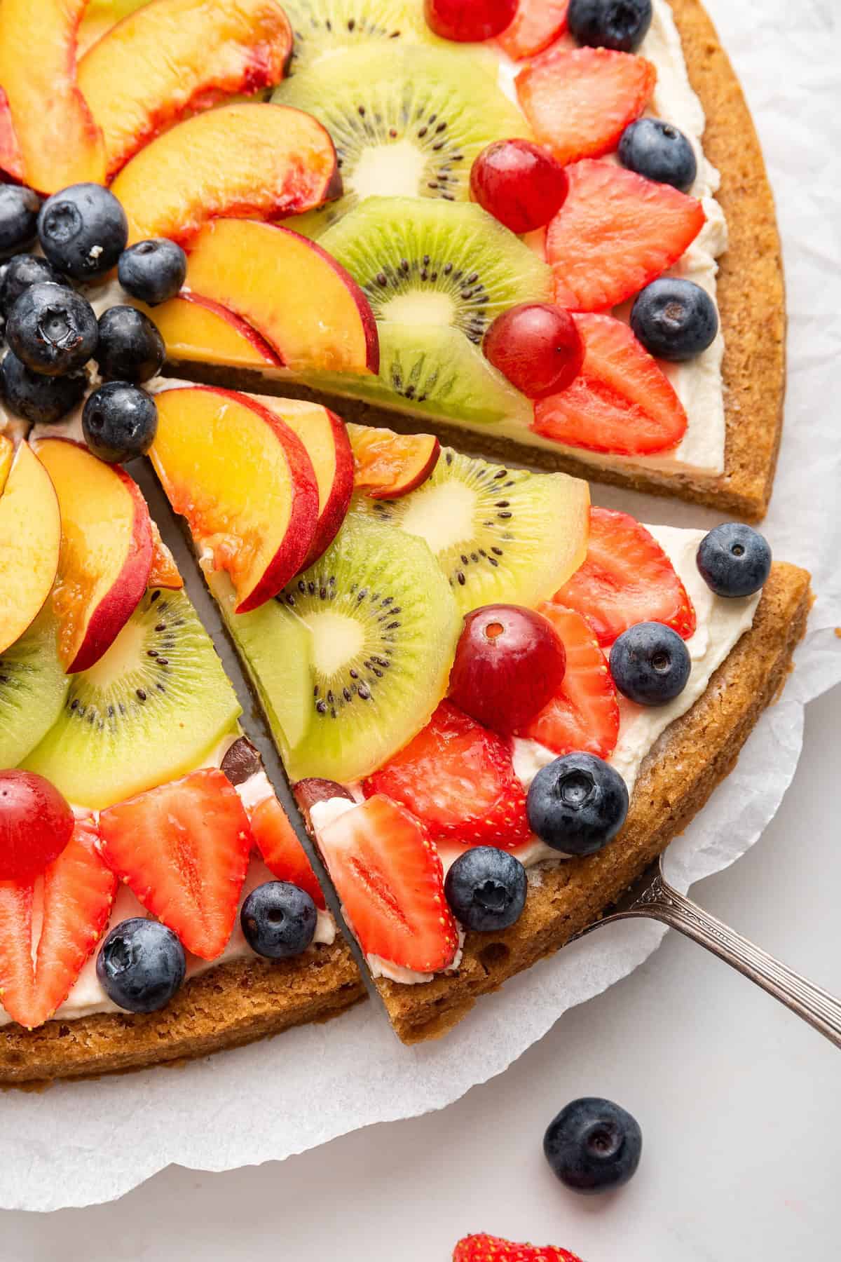 Closeup of fruit pizza on platter with one slice cut