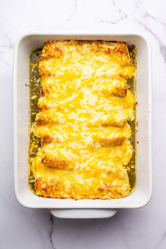 Overhead view of green chicken enchiladas in pan before garnishing