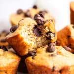 Pile of banana protein muffins with one bitten to show moist texture