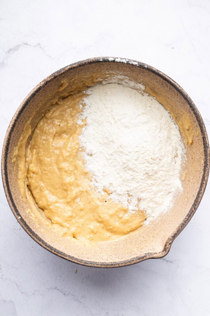 Overhead view of flour added to muffin batter in bowl