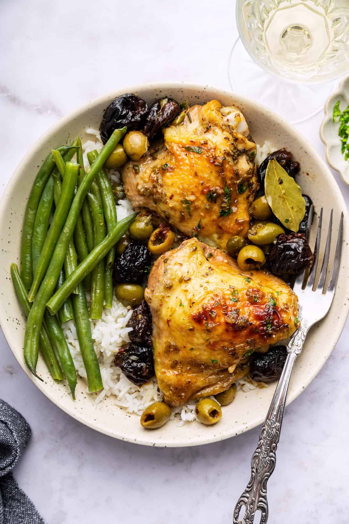 Chicken Marbella pairs juicy marinated chicken thighs with sweet prunes, olives, and capers in white wine for a mouthwatering main dish! Overhead view of chicken marbella on plate with rice and green beans