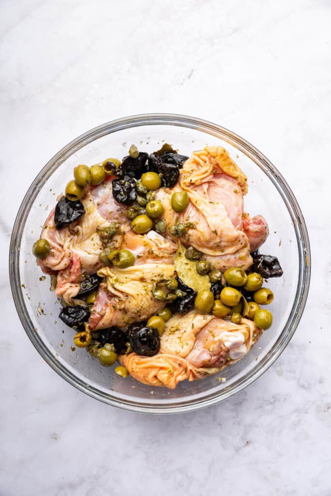 Overhead view of chicken marinating in bowl with olives and prunes