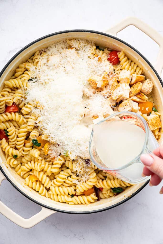 Pouring pasta water into pot of chicken pasta primavera
