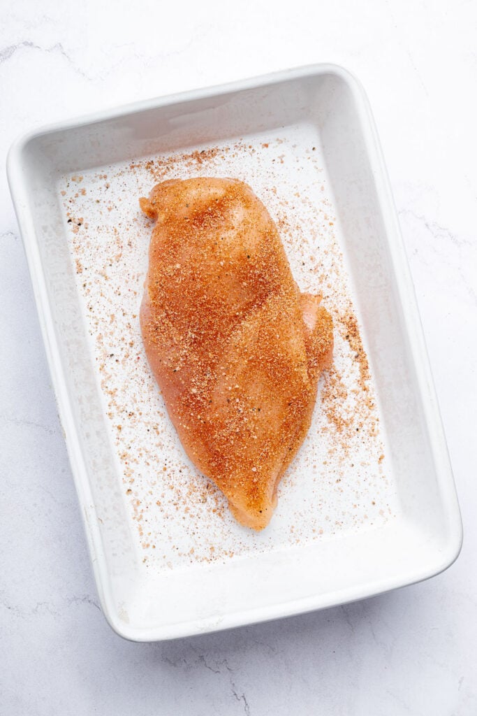 Uncooked chicken breast with seasoning in pan