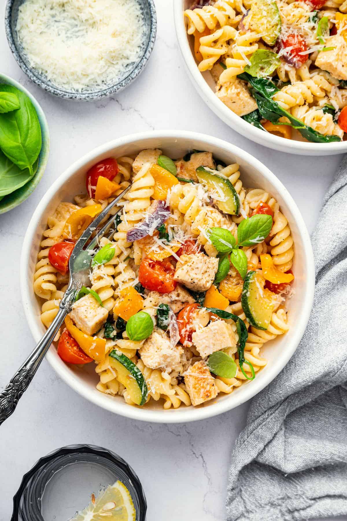 Colorful chicken pasta primavera in 2 bowls with Parmesan cheese for garnish