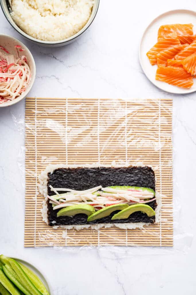 Overhead view of fillings added to rice on sushi mat