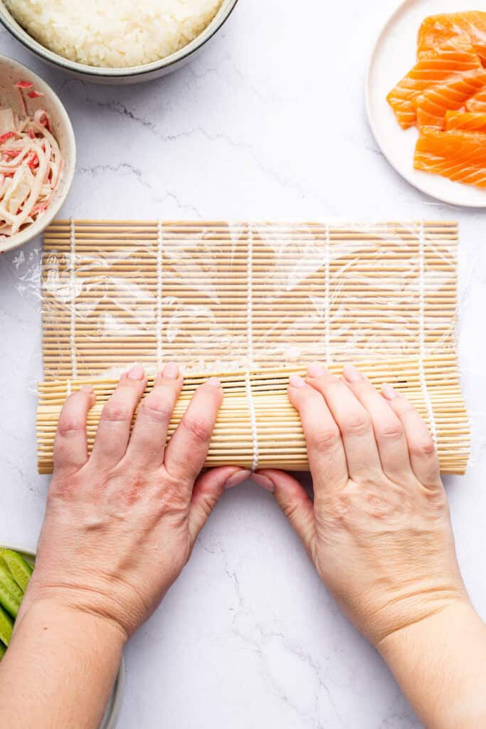 Overhead view of hands rolling Alaska roll in sushi mat