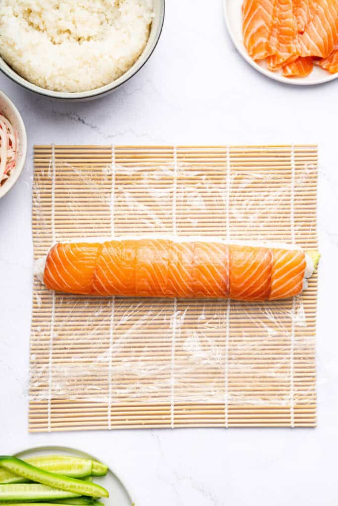 Overhead view of Alaska roll on plastic-lined sushi mat