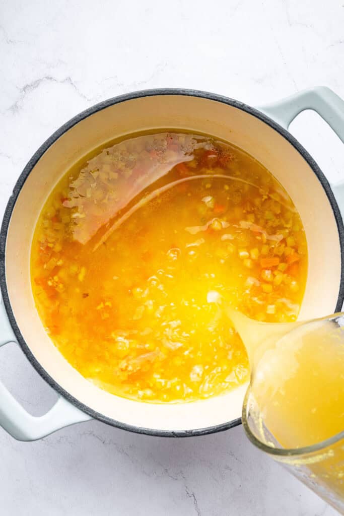 Pouring broth into pot of soup