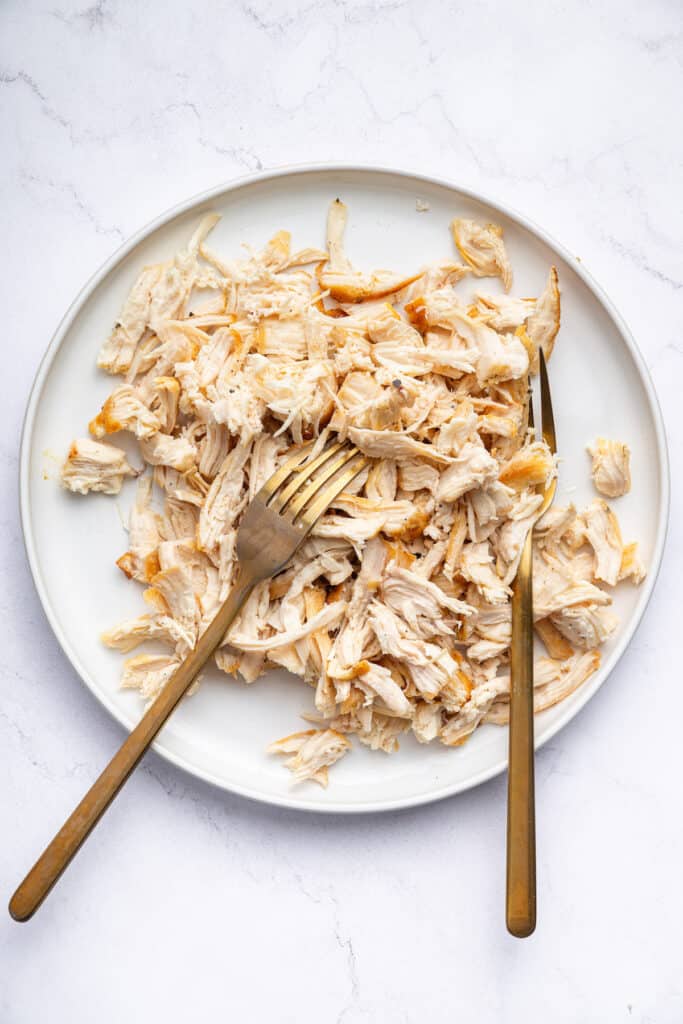 Overhead view of shredded chicken on plate with 2 forks