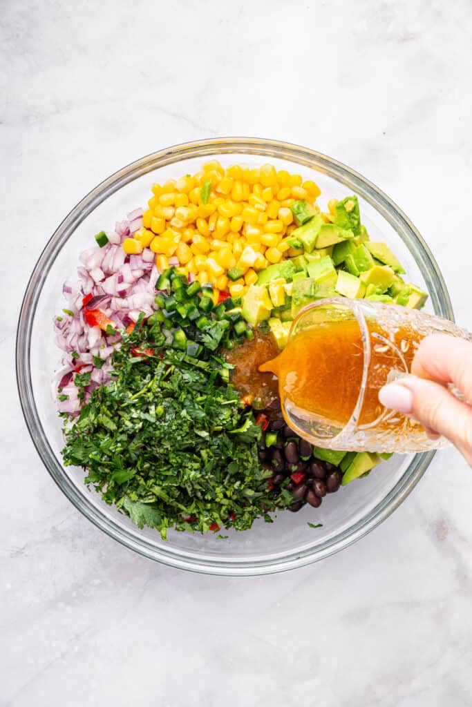 Pouring dressing into bowl of ingredients for black bean and corn salad