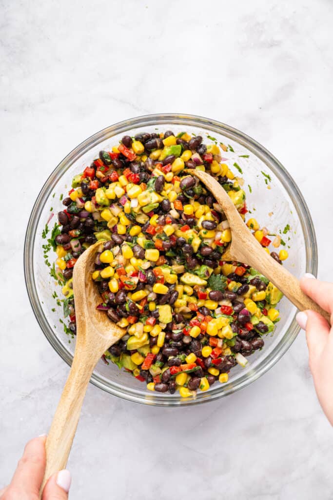 Tossing black bean and corn salad in glass bowl