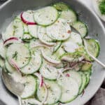 Overhead view of creamy cucumber salad in bowl with two serving spoons