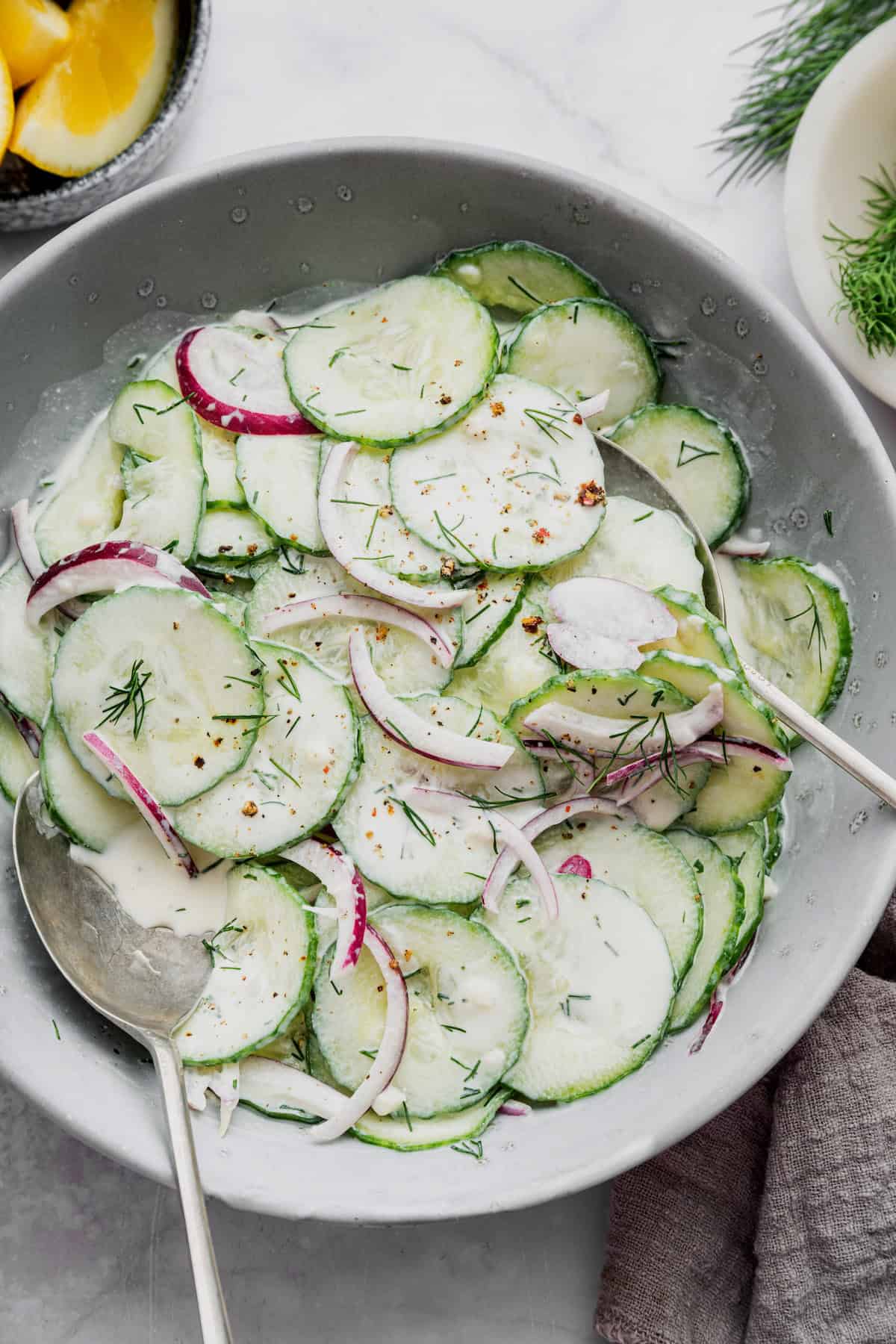 Overhead view of creamy cucumber salad in bowl with two serving spoons