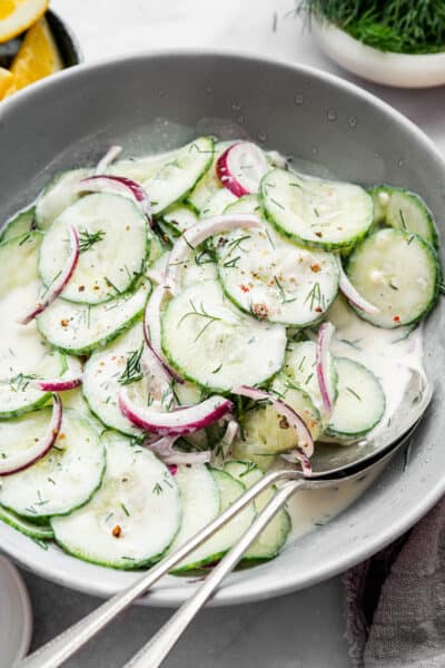 Bowl with creamy cucumber salad with two serving spoons