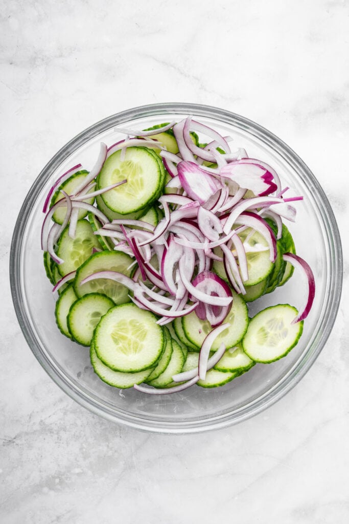 Overhead view of cucumbers and red onion in glass bowl
