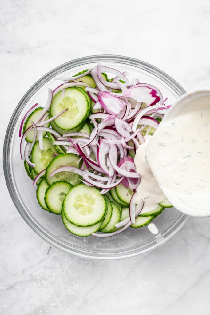 Pouring dressing into bowl of cucumbers and onion
