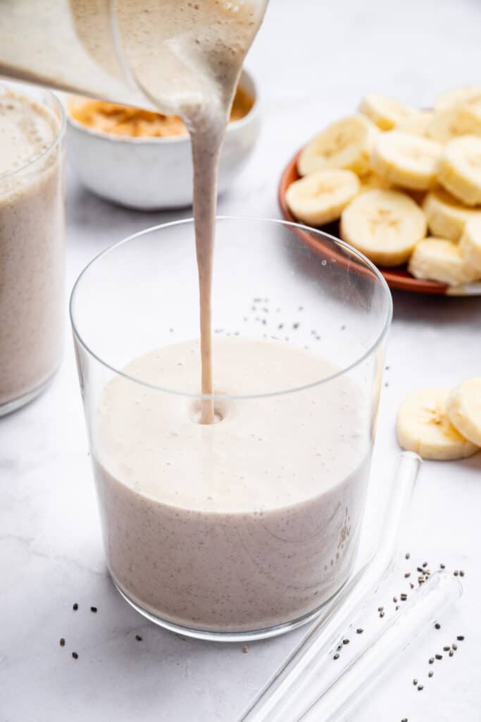 Pouring peanut butter banana smoothie into glass