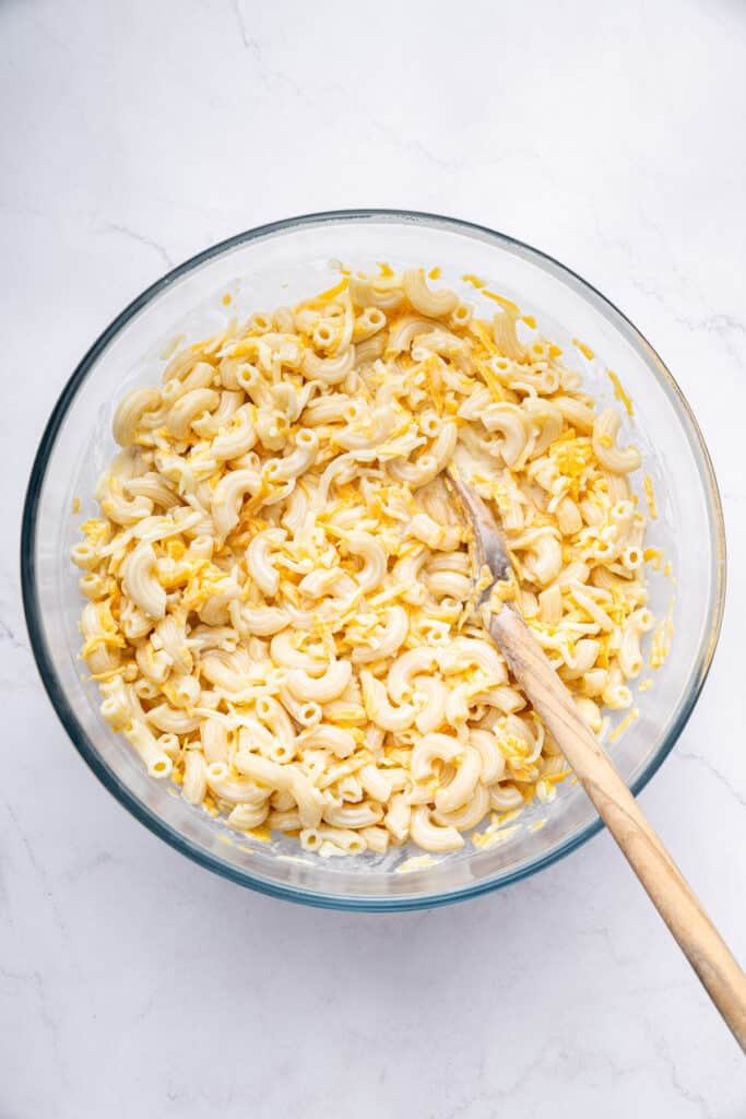 Overhead view of cheese sauce and pasta being stirred in bowl