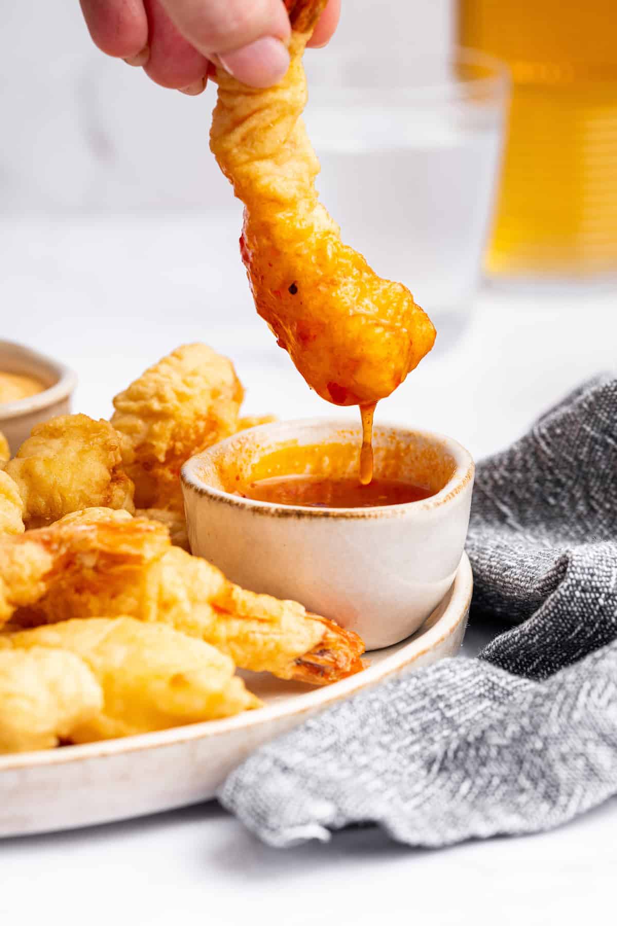 Dipping shrimp tempura into bowl of sauce