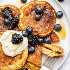 Overhead view of cottage cheese pancakes on plate with yogurt, berries, and maple syrup