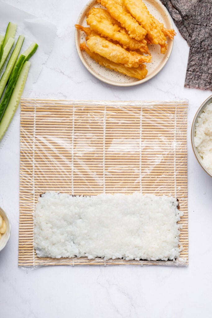 Overhead view of nori topped with rice on sushi mat