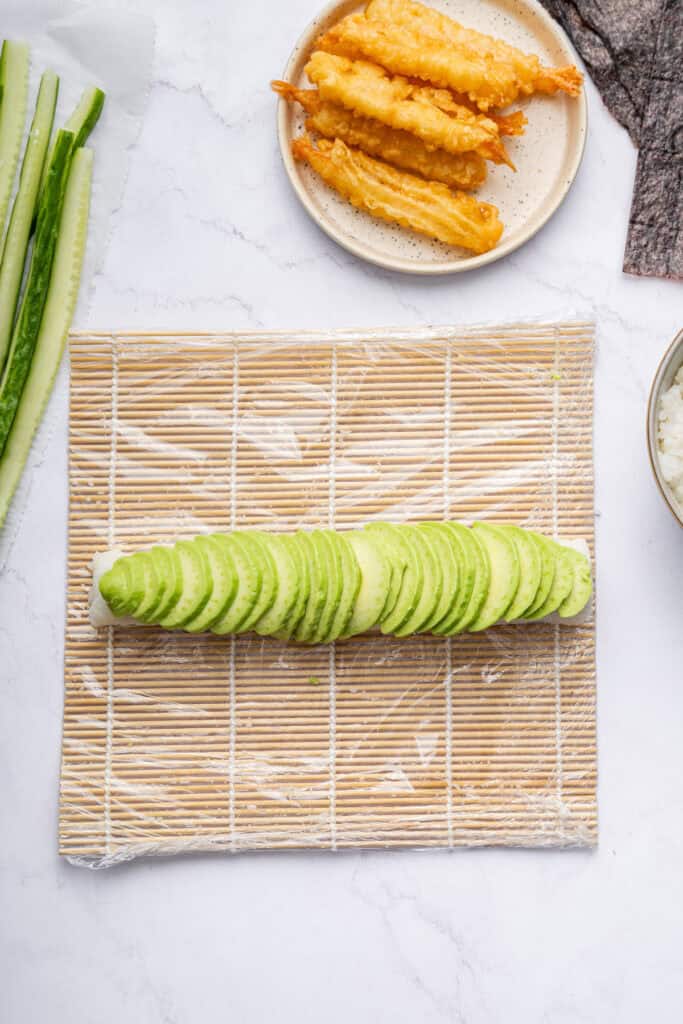 Overhead view of sliced avocado placed onto rice for dragon roll