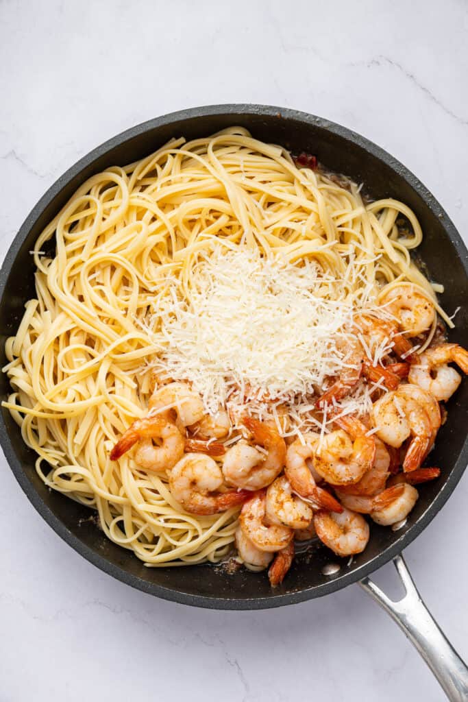 Overhead view of pasta, shrimp, and cheese added to skillet