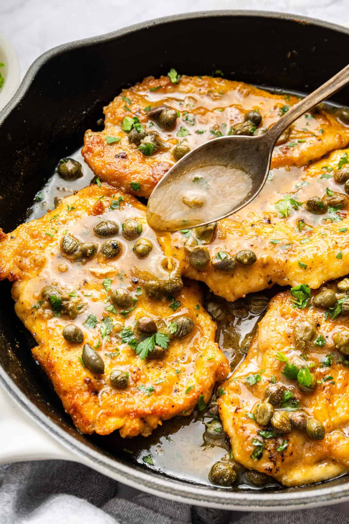 Spooning sauce over lemon caper chicken in skillet