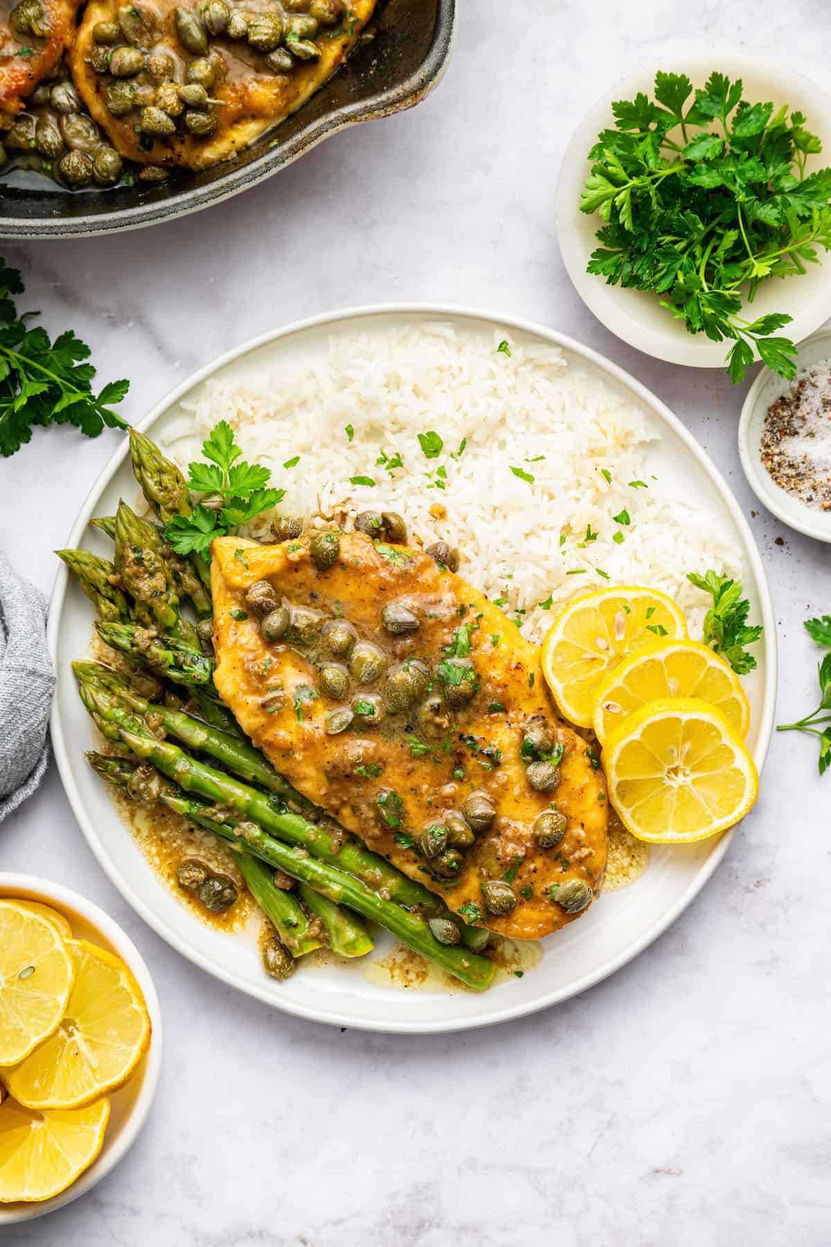 Overhead view of lemon caper chicken on plate with white rice, lemon slices and asparagus