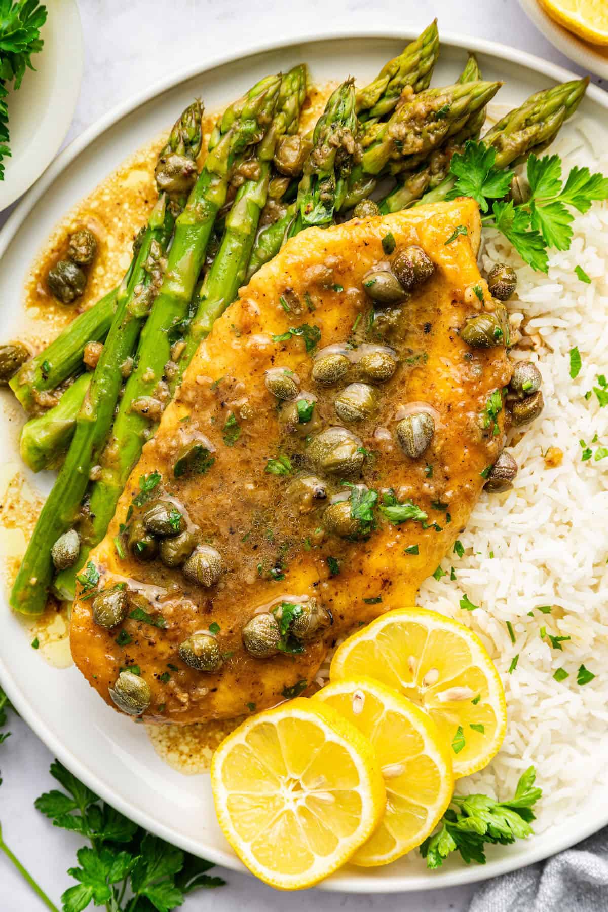 This lemon caper chicken is tender and juicy, full of bright flavor, and ready in under 30 minutes. It tastes like it came from a restaurant! Lemon caper chicken on plate with rice and asparagus