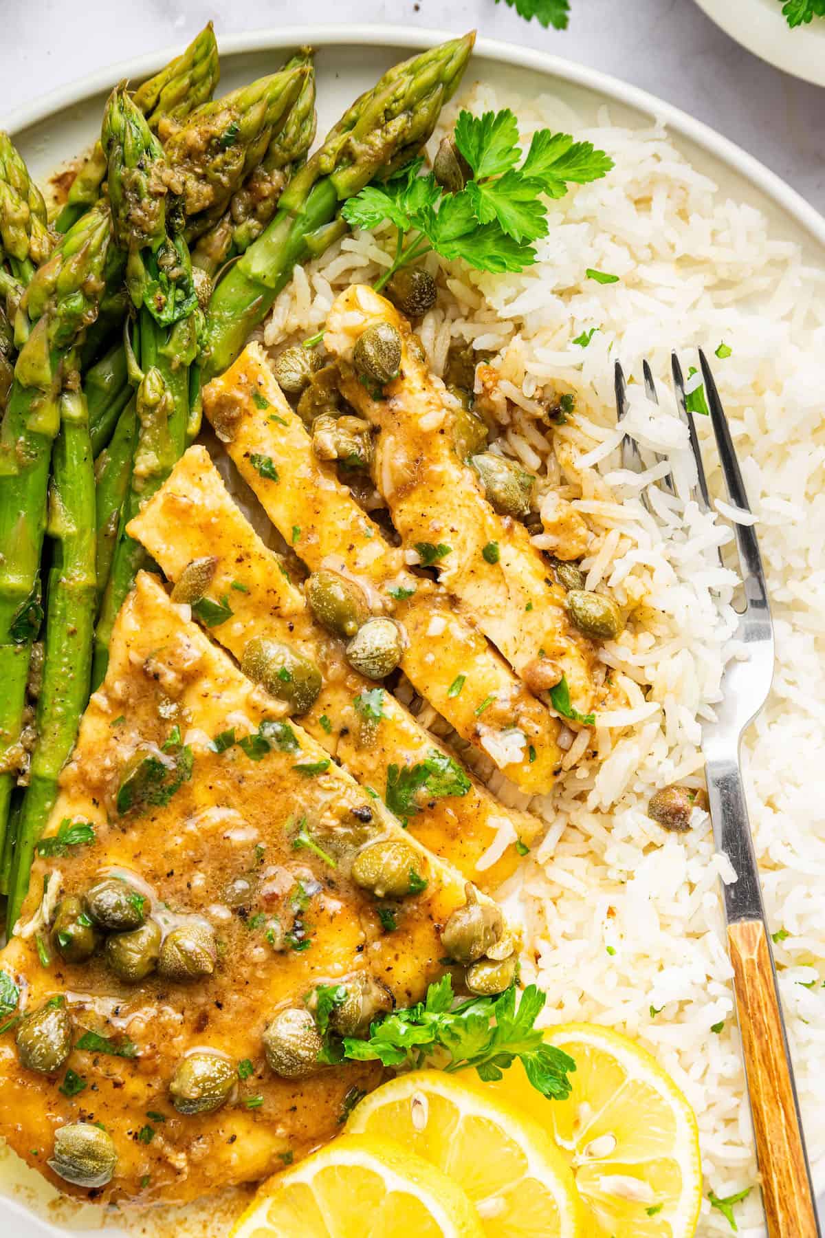 Overhead view of sliced lemon caper chicken on plate with rice and asparagus
