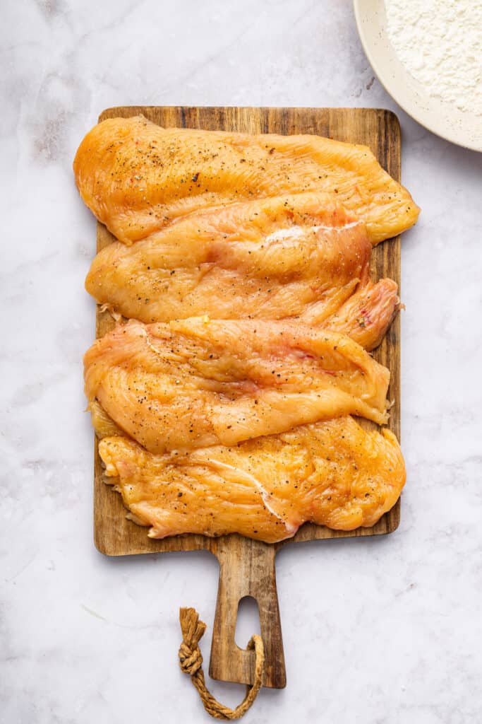 Overhead view of seasoned chicken cutlets on wooden board